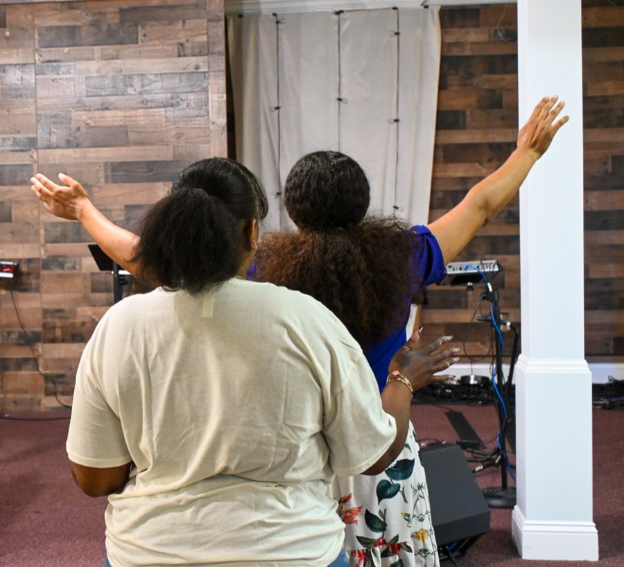 Two women standing arm in arm with hands raised during worship.